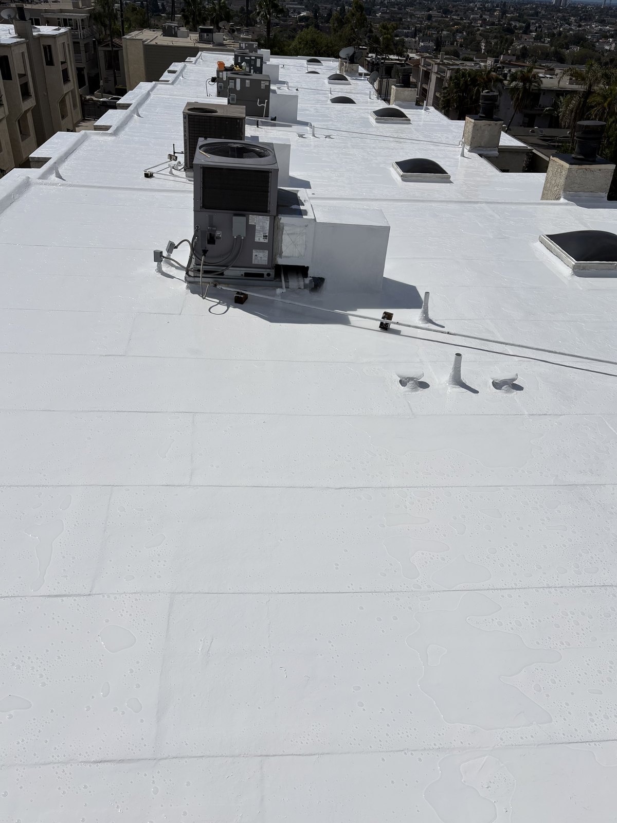 Completed white silicone roof restoration surface with rooftop HVAC equipment in Signal Hill.