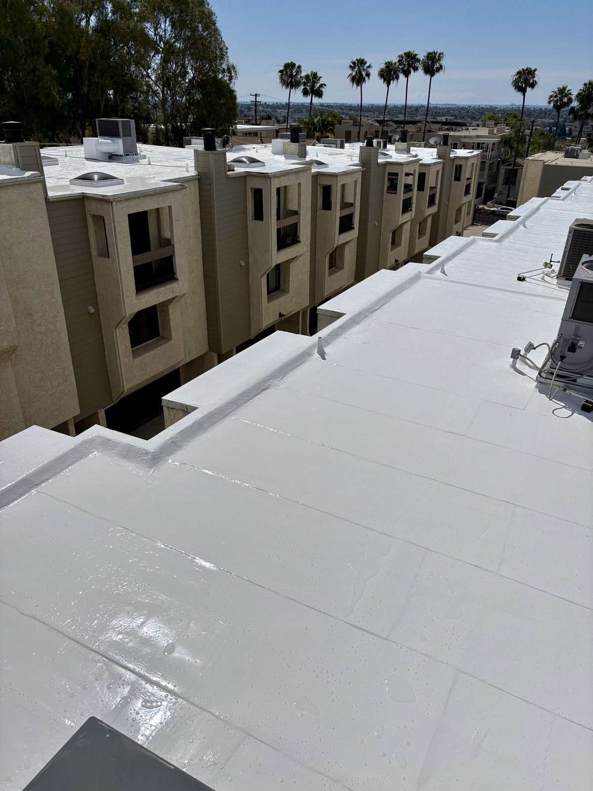 Finished white silicone roof coating on a multi-family HOA building in Signal Hill.